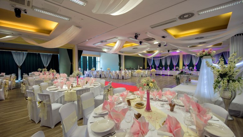 Large banqueting hall with many tables and a laid table.