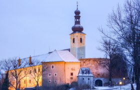 Gloggnitz Castle in winter with illuminated tower and snow-covered roof.
