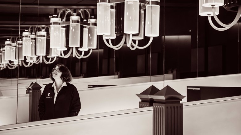 A woman stands in a room with large, modern chandeliers and mirrors.