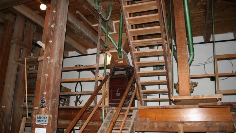 Interior view of an old mill with wooden stairs and machinery.