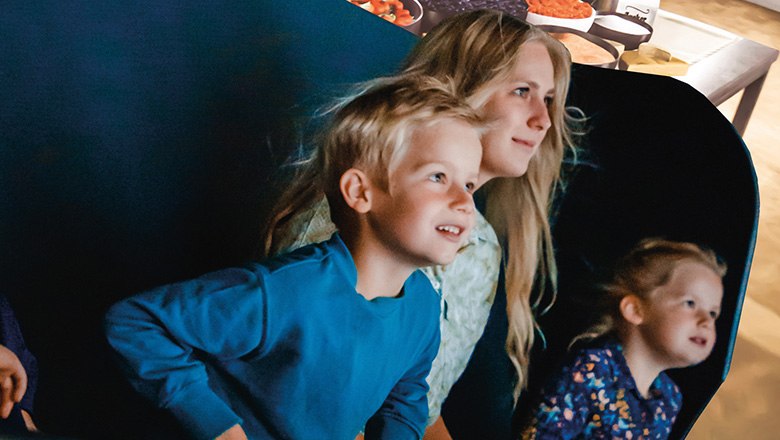 Two children and a woman sit in a carriage in the Flying Theater and look ahead, spellbound.