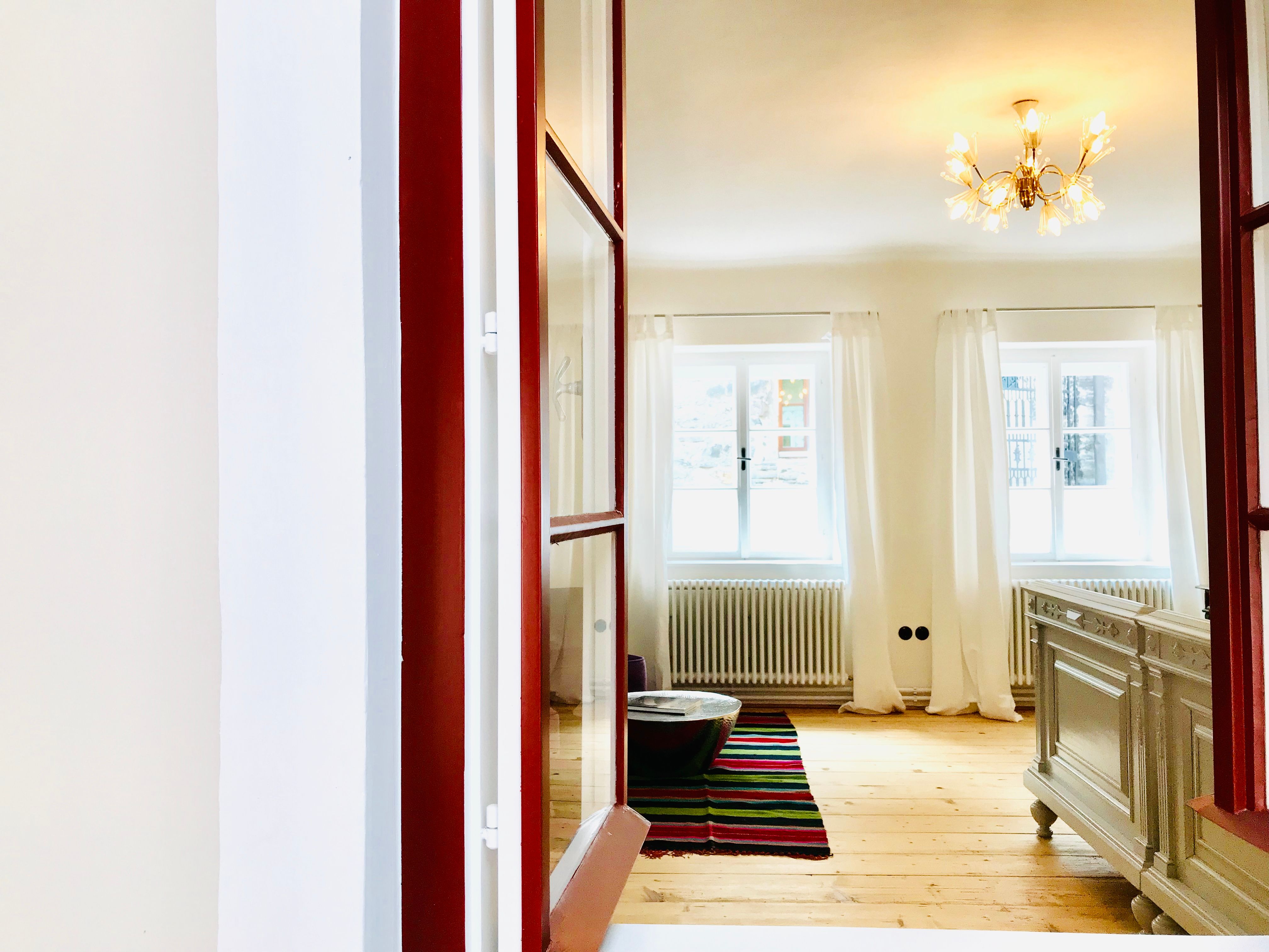 Bright bedroom with wooden floor, white curtains and a chandelier.