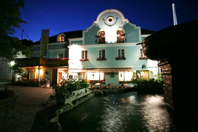 A traditional inn with a blue façade and illuminated windows at night, with a fountain in the foreground.