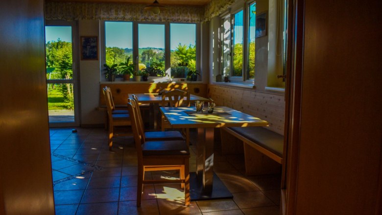 A cozy breakfast room with wooden furniture and large windows that let in sunlight.