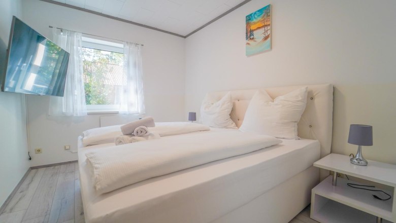 Modern bedroom with double bed, white bed linen, mural, window with curtains and flat screen TV.