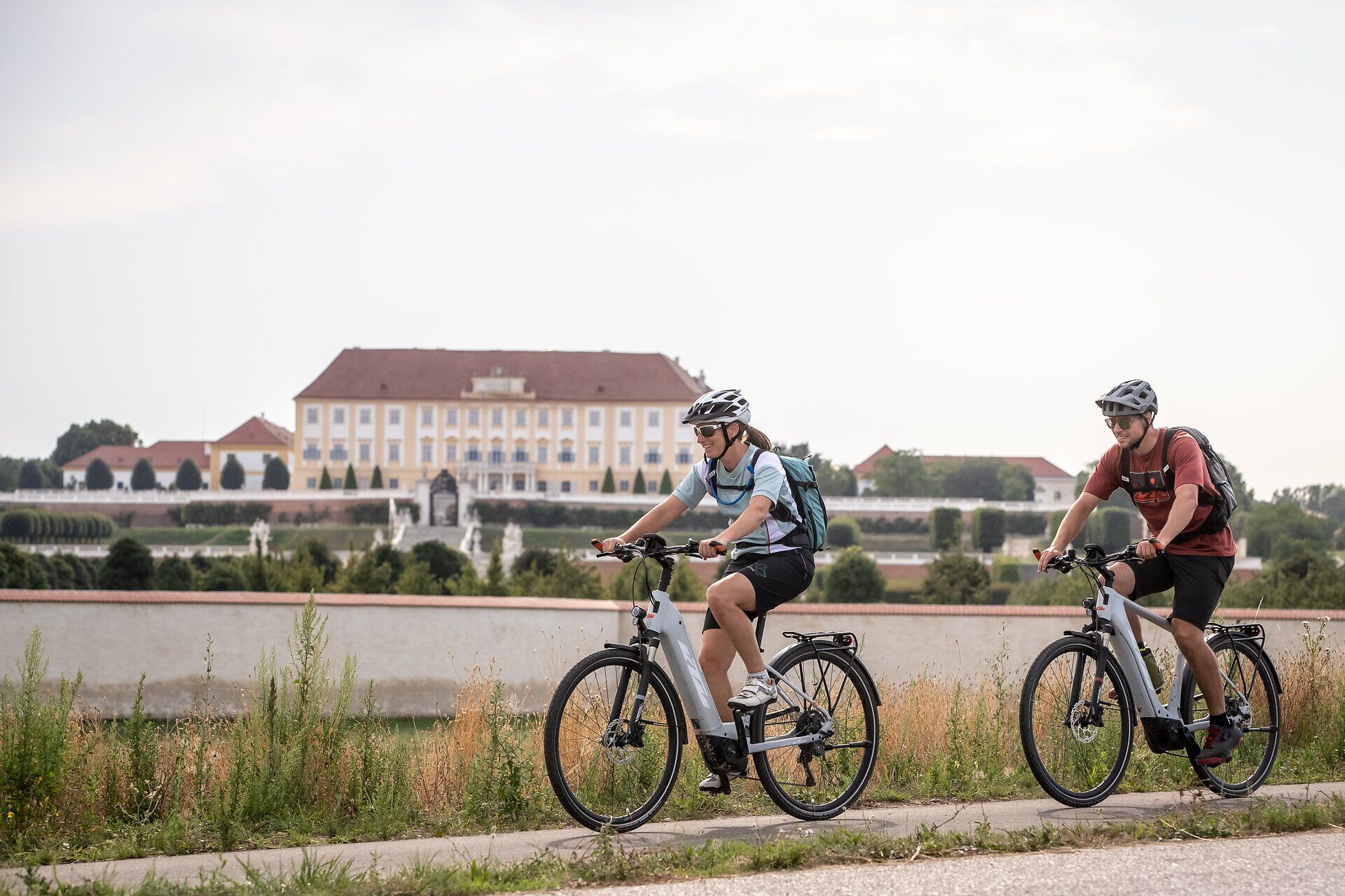 Two cyclists enjoy the fresh air and picturesque scenery along a quiet canal. The rolling hills in the background and the lush vegetation create an inviting atmosphere for outdoor enthusiasts. This is summer at its best.