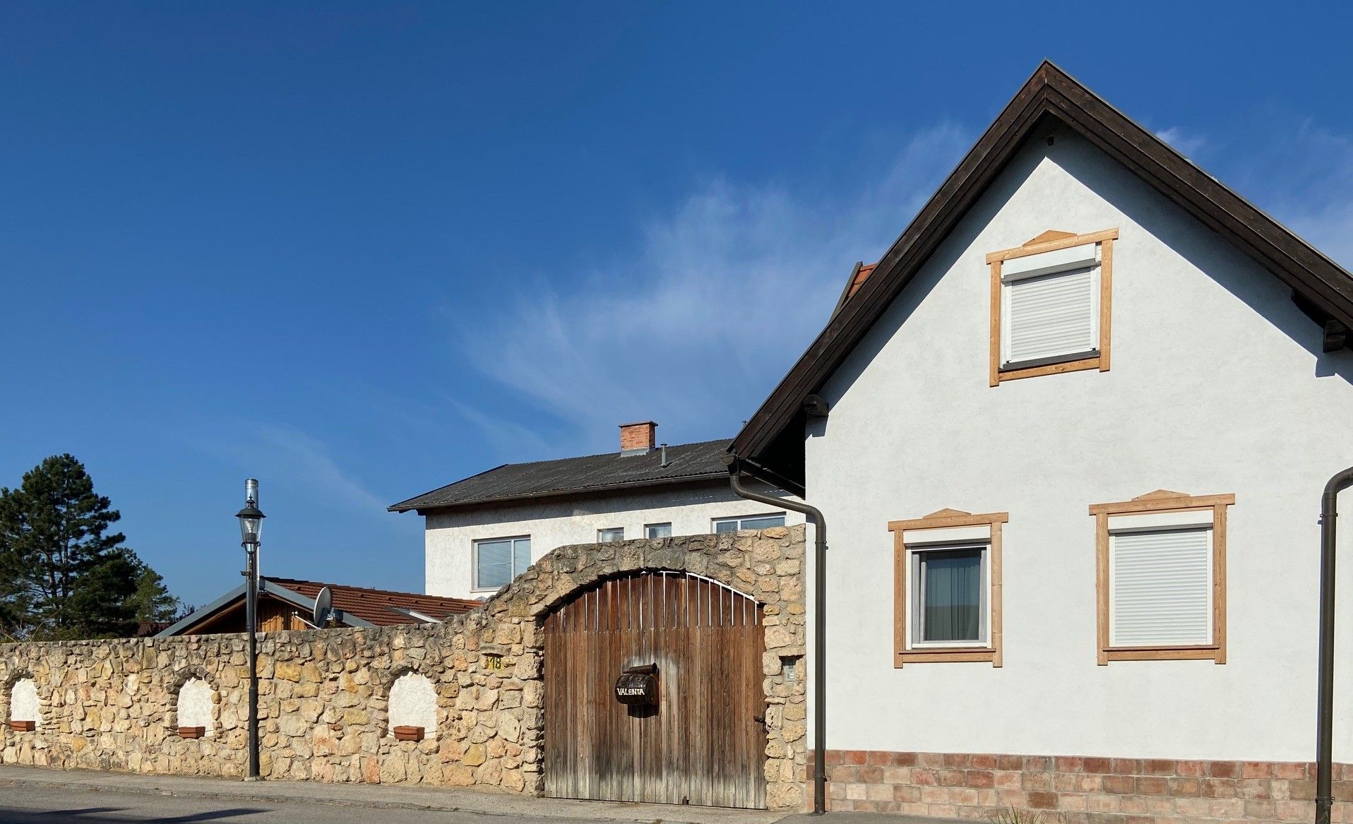 A white house with brown window frames and a stone wall with a wooden gate under a blue sky.