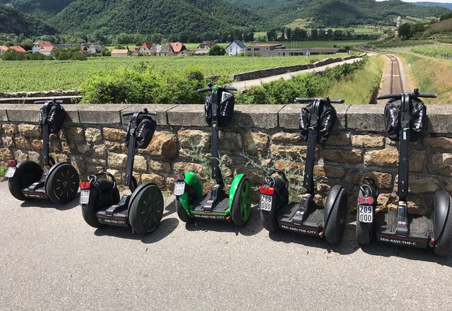 Six Segways stand in front of a stone wall with a landscape in the background.
