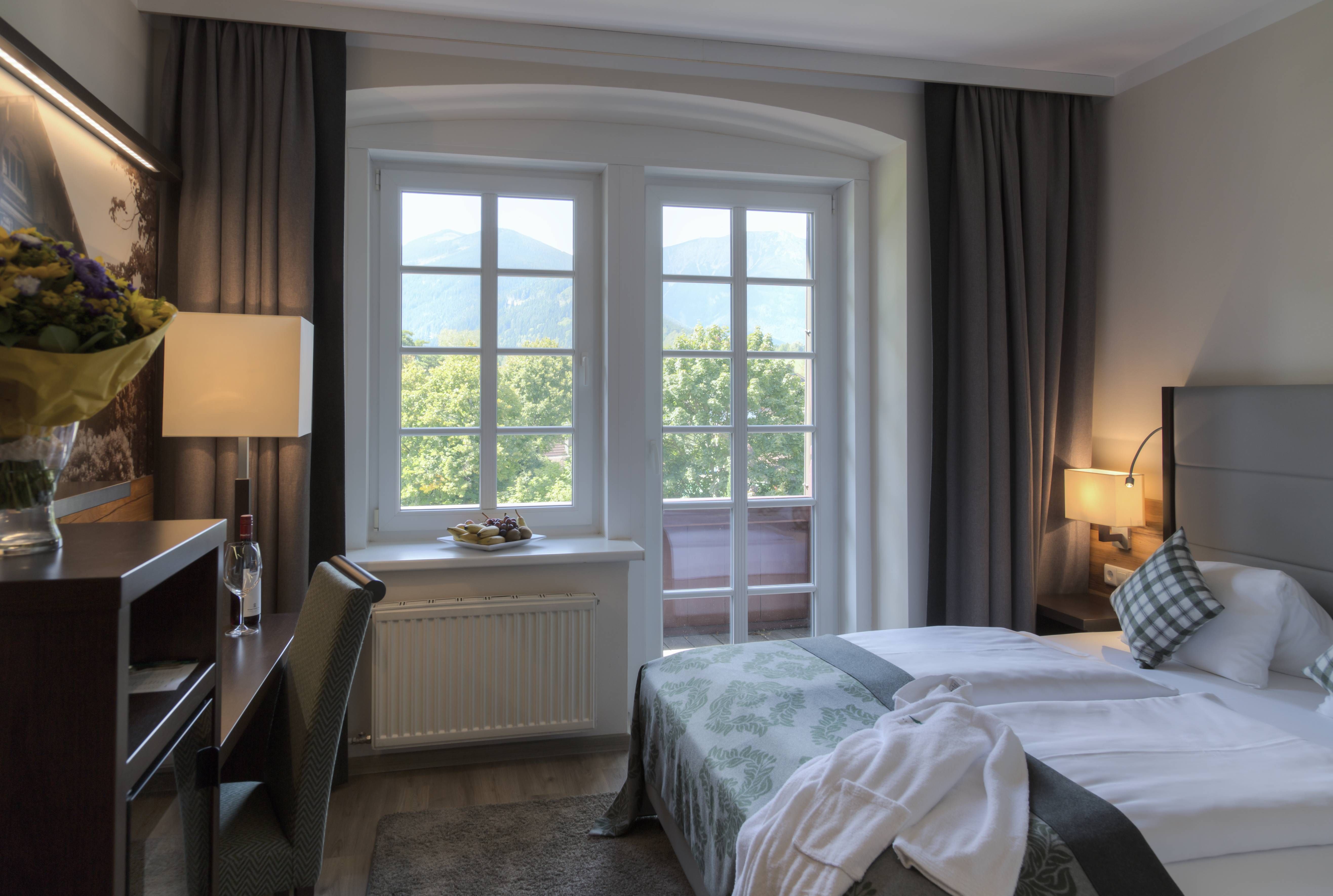 A cozy hotel room with double bed, window with mountain view, desk and flowers.