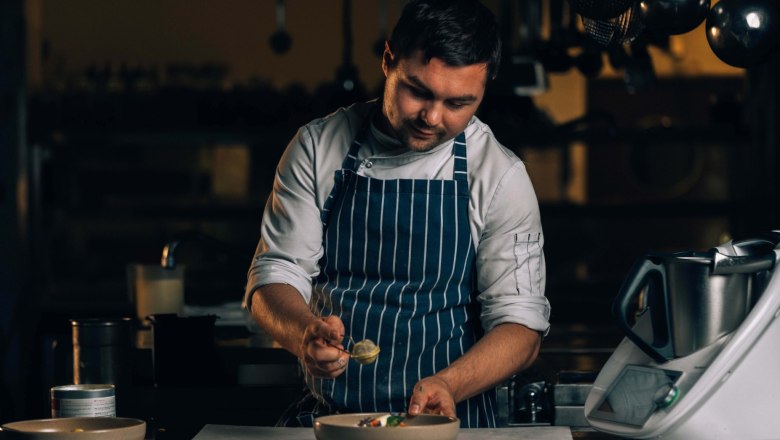 A chef in a striped apron prepares a dish in a kitchen.