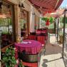 Outdoor terrace of a café with red tables and chairs under a striped awning.