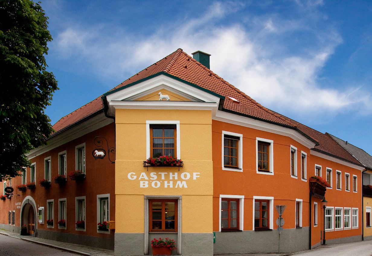 A traditional inn with an orange and yellow façade and red roof tiles under a blue sky.