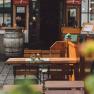 An empty table with wooden chairs in a guest garden, in the background a wine barrel and an entrance.