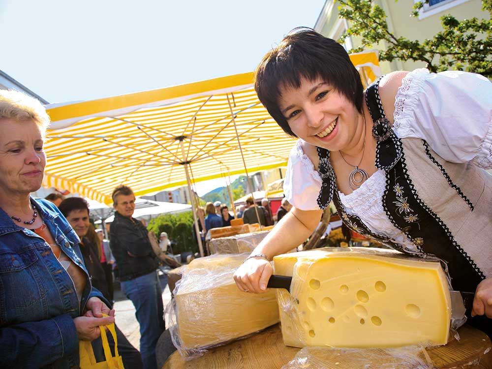 Woman in traditional dress cutting cheese at a market.