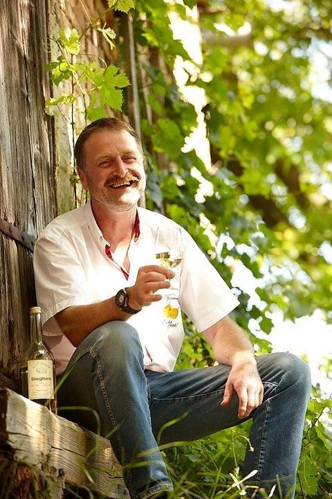 Man sitting outside with a glass of wine in his hand, surrounded by green plants.