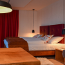 Cozy hotel room with double bed, red curtains and wooden furniture.