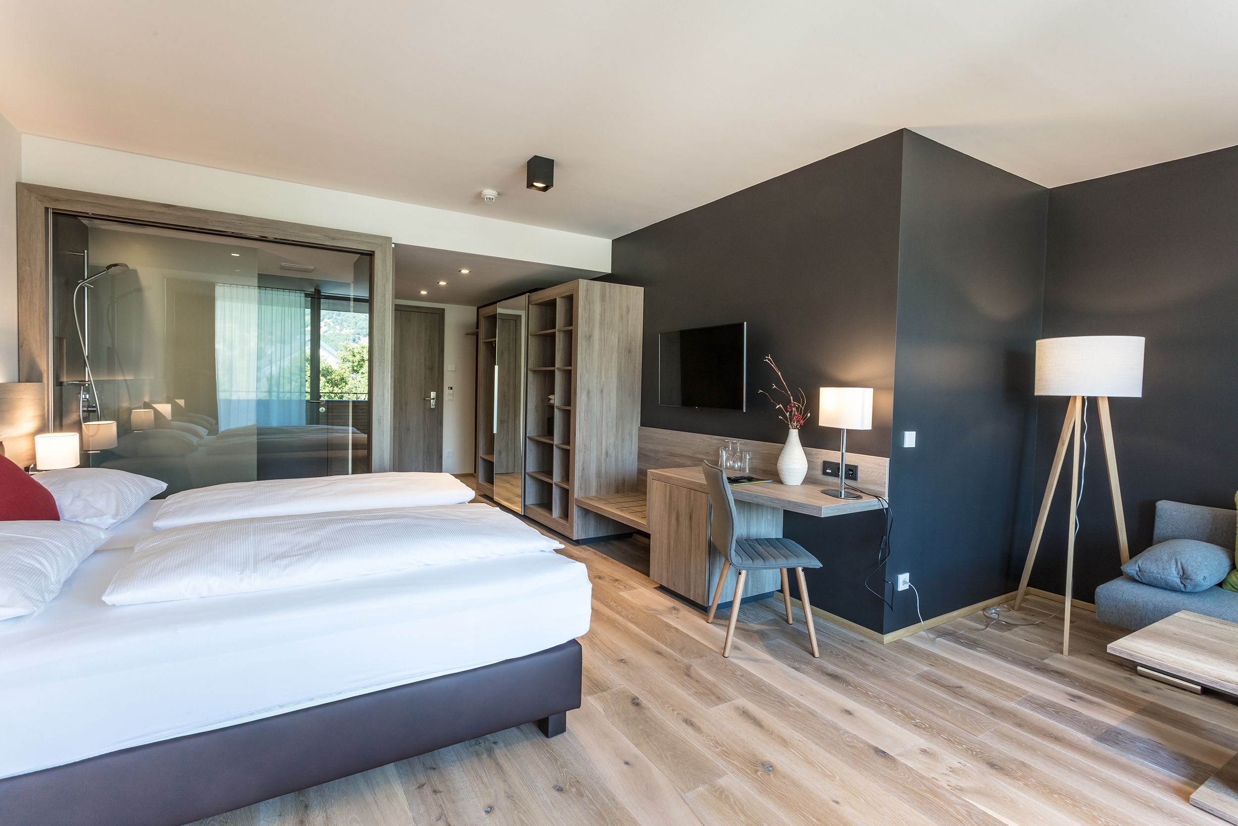 Modern hotel room with double bed, desk, TV and glass shower.