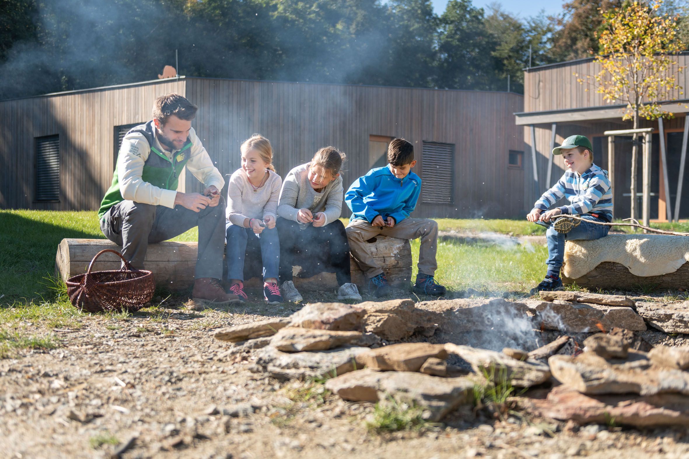 Group of children and an adult around an outdoor campfire.