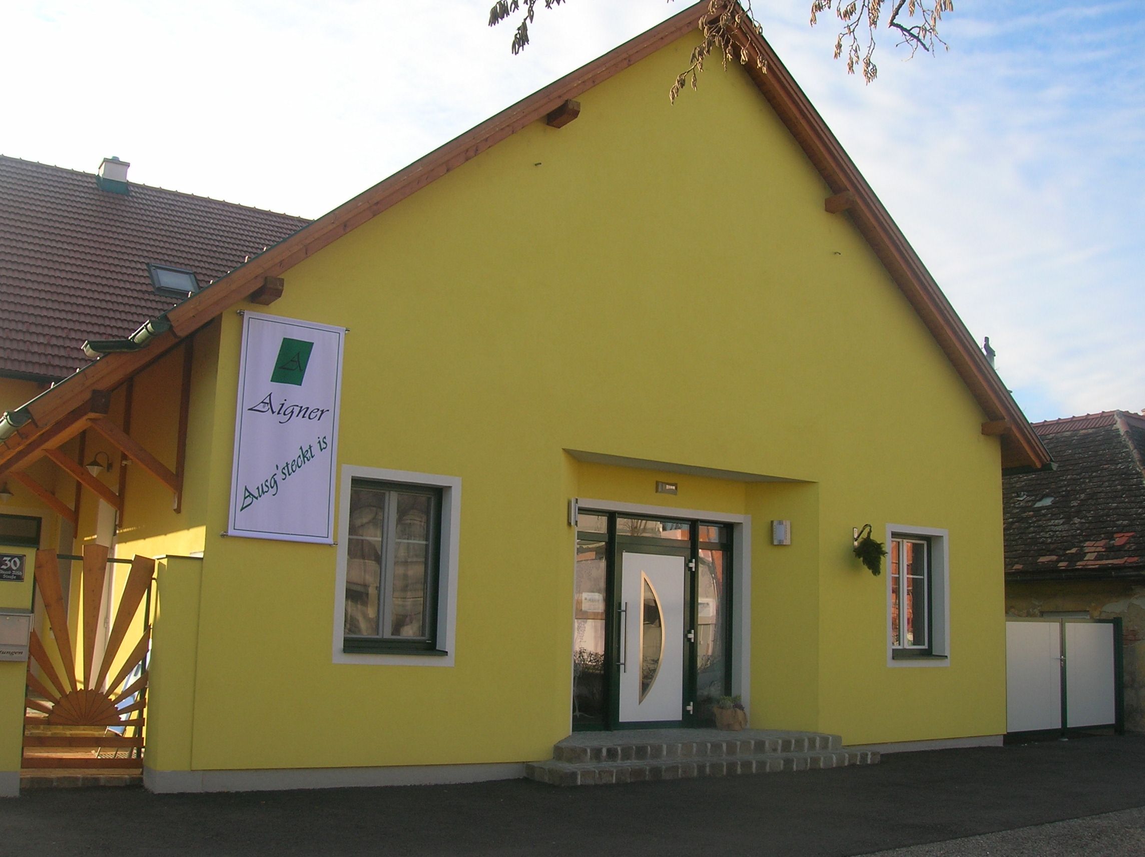 Yellow building with a sign "Aigner Ausg'steckt is" on the façade.