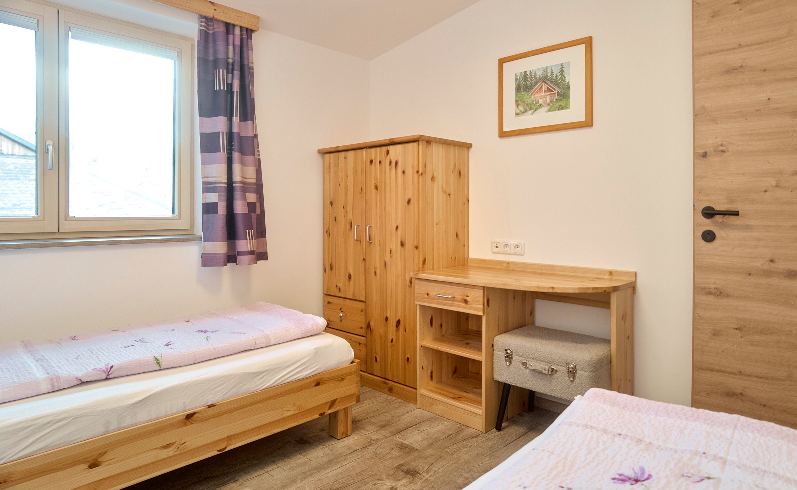Children's room with two single beds, wooden furniture and a window with purple curtains.