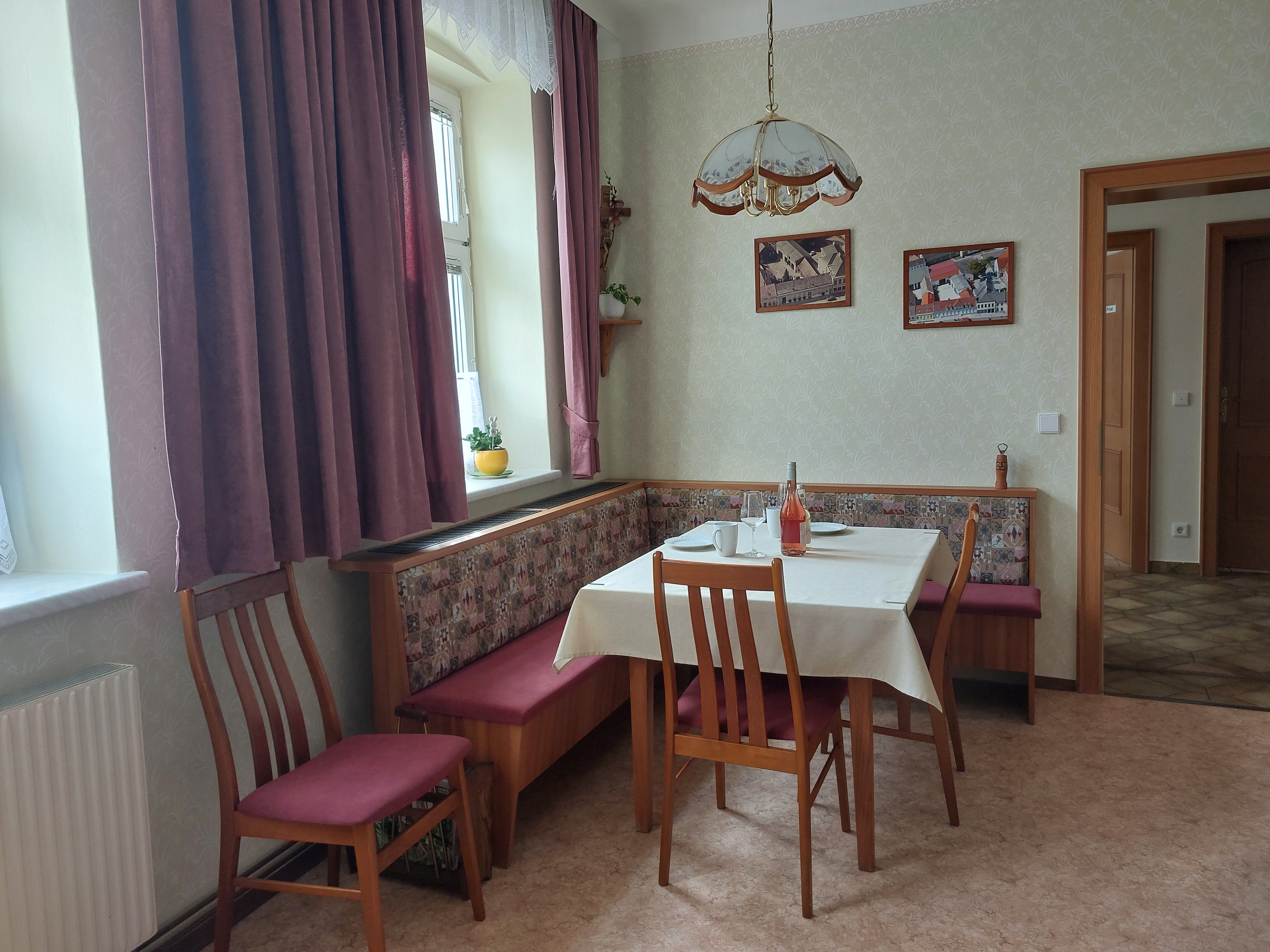 Cozy eat-in kitchen with dining table, chairs and corner bench. Window with curtains, pictures on the wall.
