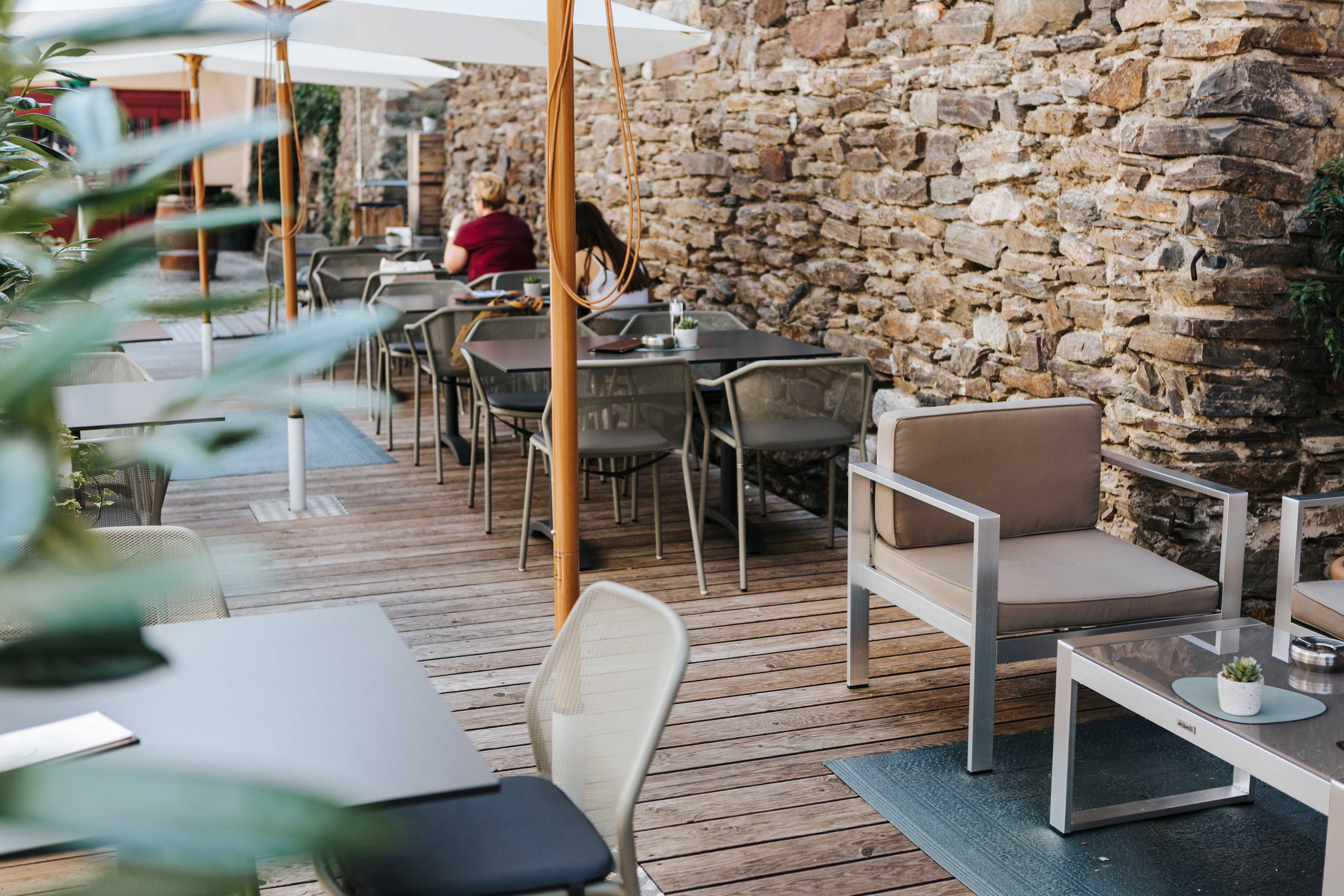 Cozy outdoor area of a café with wooden floor, modern furniture and stone wall.