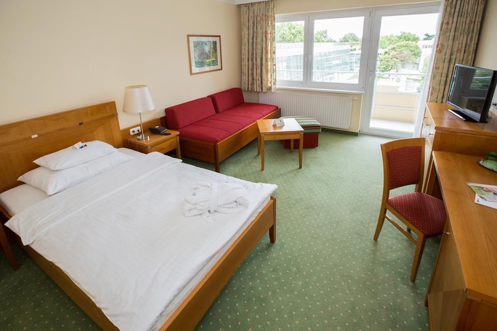 Hotel room with double bed, red sofa, desk and balcony.