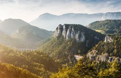 Die sanften Hügel und majestätischen Berge laden zu unvergesslichen Erlebnissen in der Natur ein. Ein sanfter Nebel umhüllt die Landschaft und verleiht der Szenerie eine mystische Atmosphäre, während die Sonne langsam aufgeht und die Farben der Natur zum Leben erweckt.