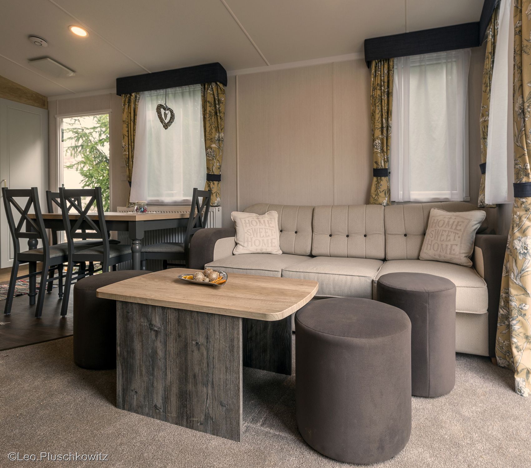 Cozy living room with beige couch, wooden table and dining area in the background.