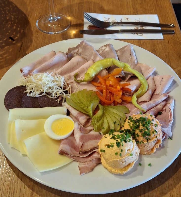 A snack plate with various types of sausage and cheese, egg, peppers, gherkins and spread on a wooden table.