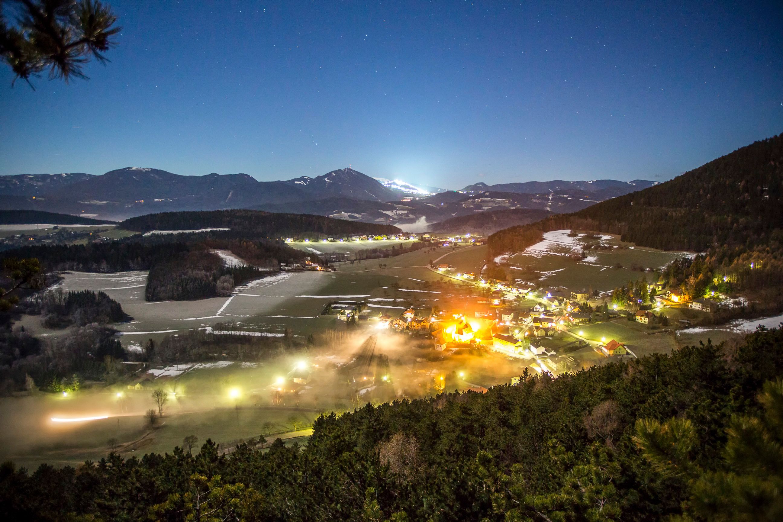Nocturnal landscape view of Prigglitz with illuminated houses and mountains in the background.