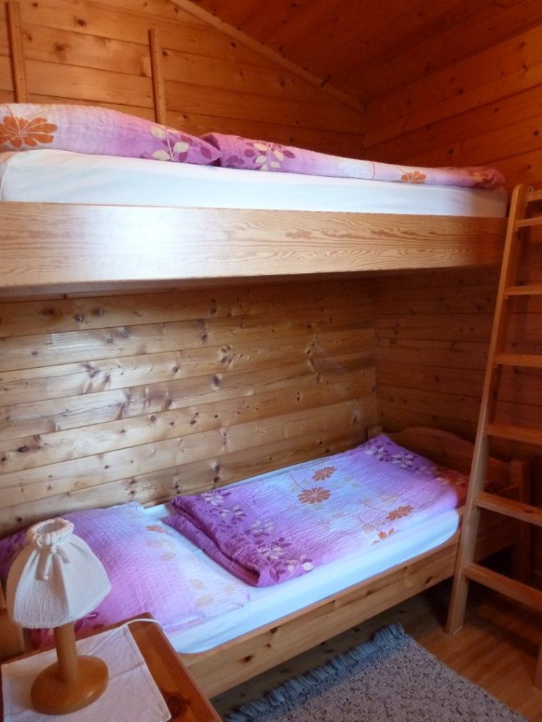 Interior view of a wooden holiday home with bunk beds and purple bedding.