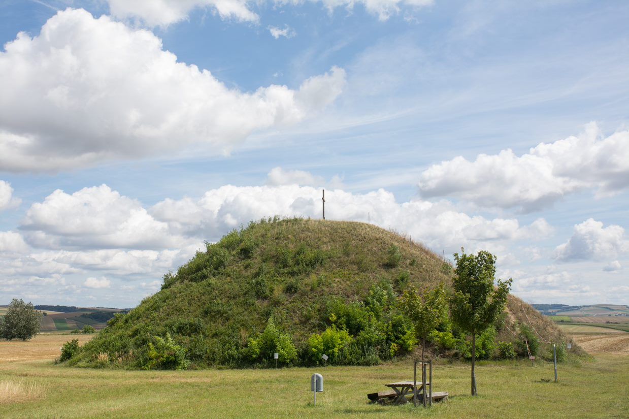 A grassy hill with a cross on top under a cloudy sky.