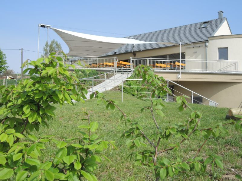 Wine tavern with terrace and awning, surrounded by green countryside.