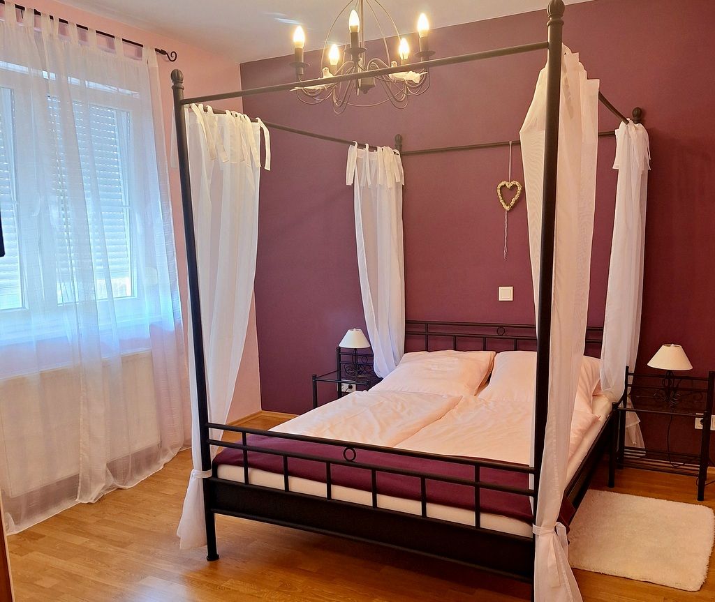Bedroom with four-poster bed, purple walls and white curtains.