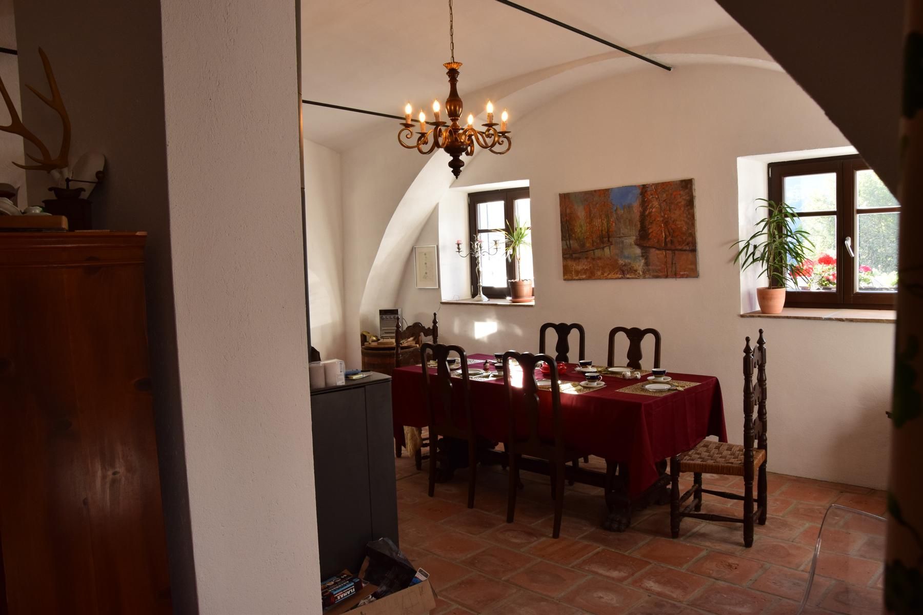 A dining room with a table set with a red tablecloth. A painting hangs on the wall and a chandelier hangs from the ceiling.