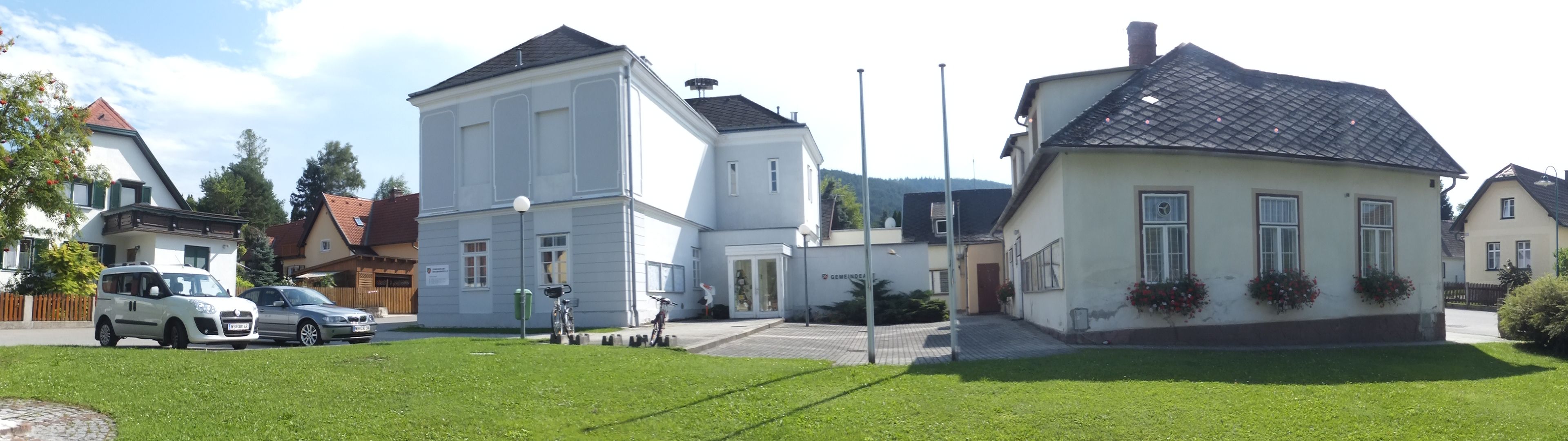 Panoramic picture of the Waidmannsfeld municipal office with surrounding buildings and cars.