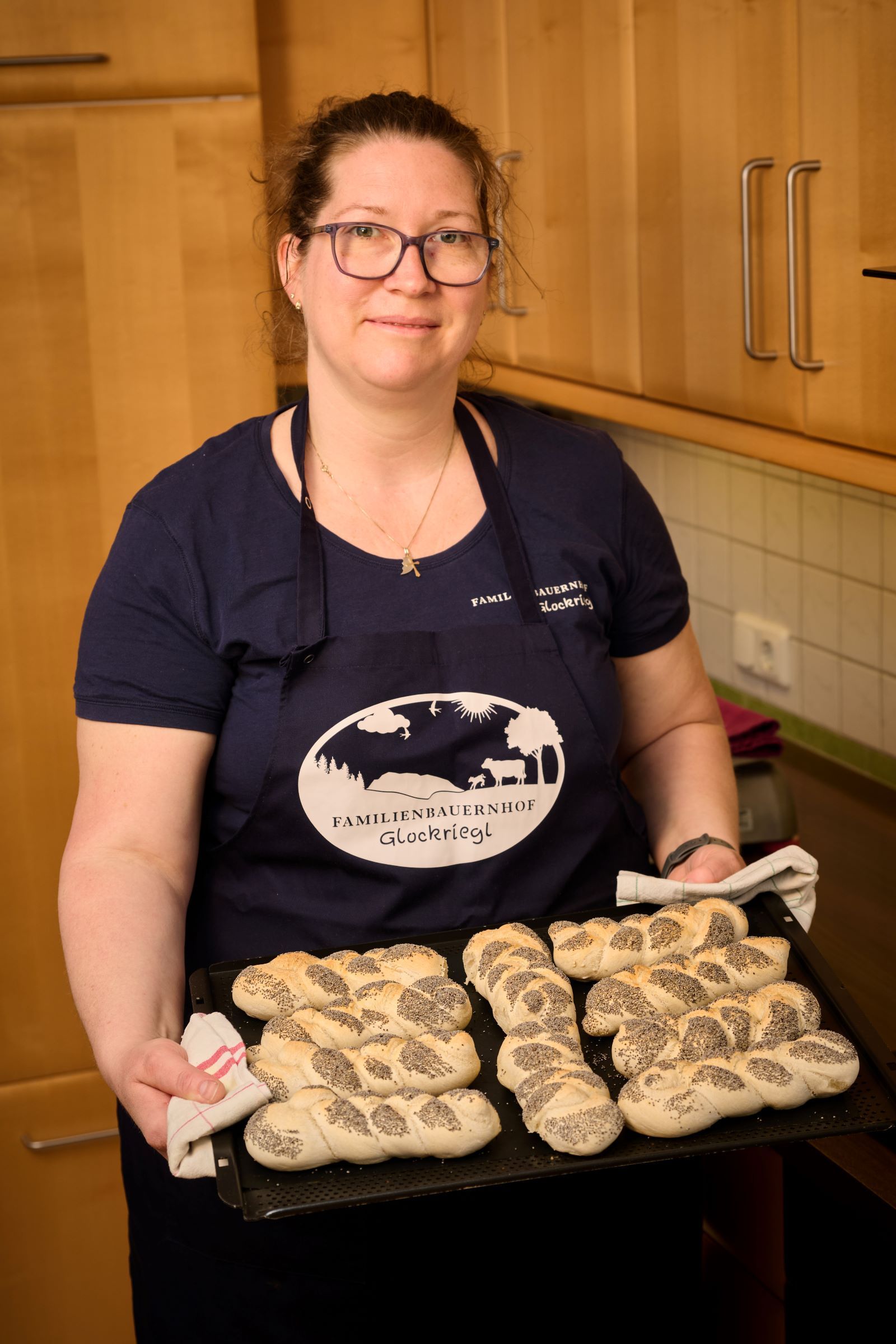 A woman in a kitchen holds a tray of freshly baked poppy seed rolls.