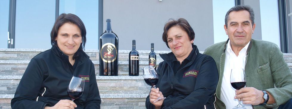 Three people sit on steps with wine glasses and bottles of wine.