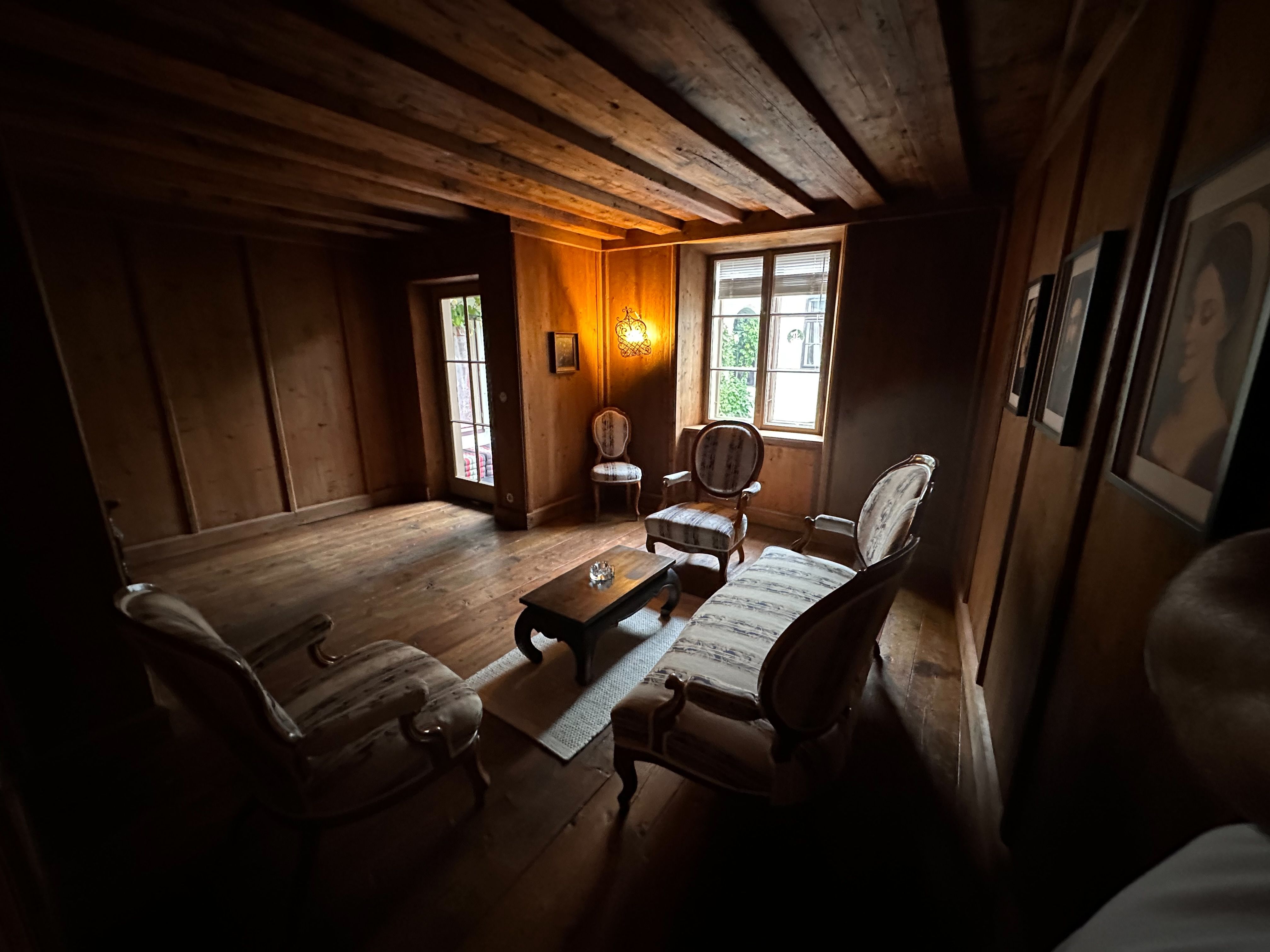 A cozy men's room with wooden walls, antique furniture and a window.