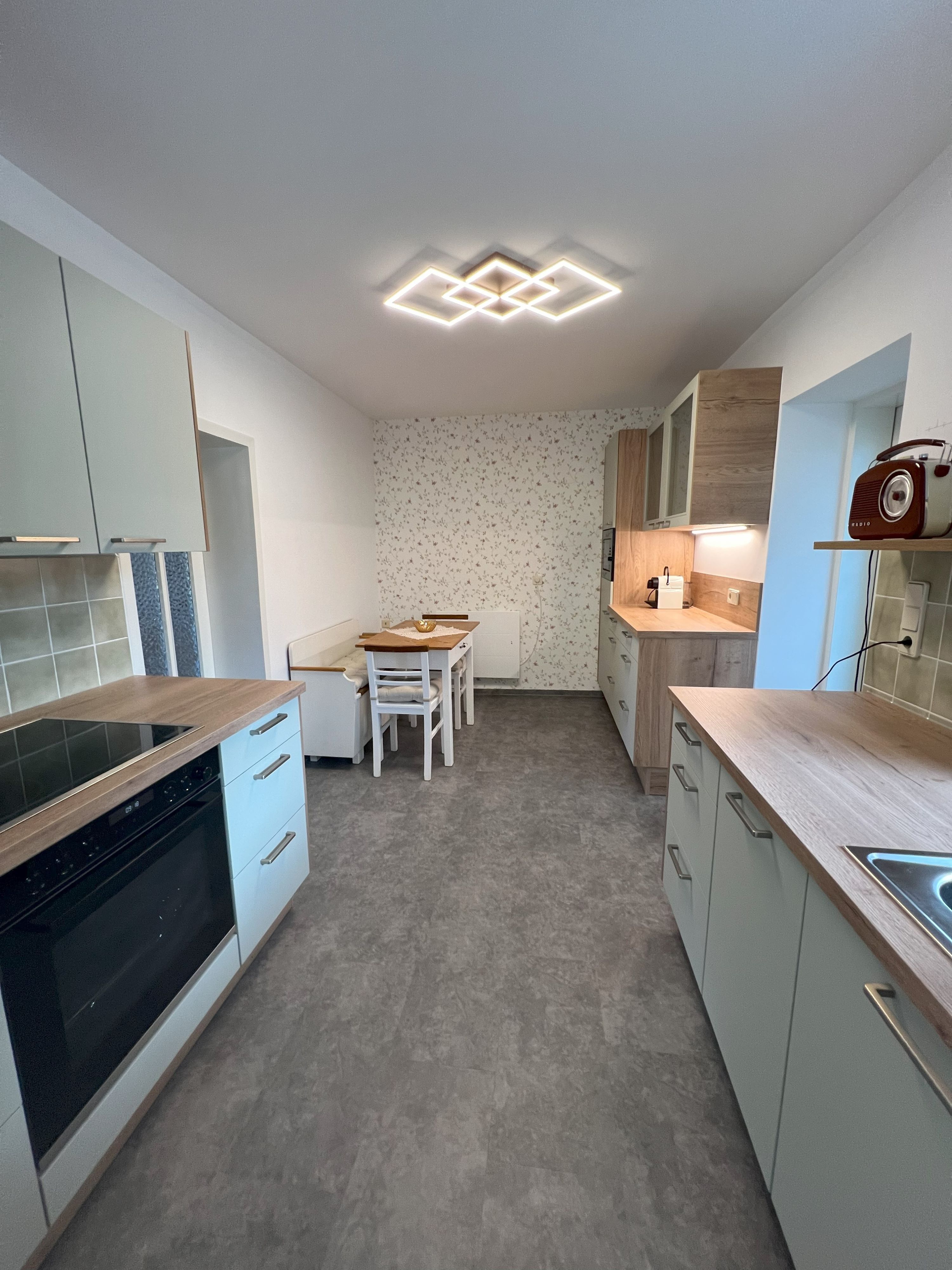 Modern kitchen with gray cabinets, wooden accents and a dining table. A geometric lamp on the ceiling.