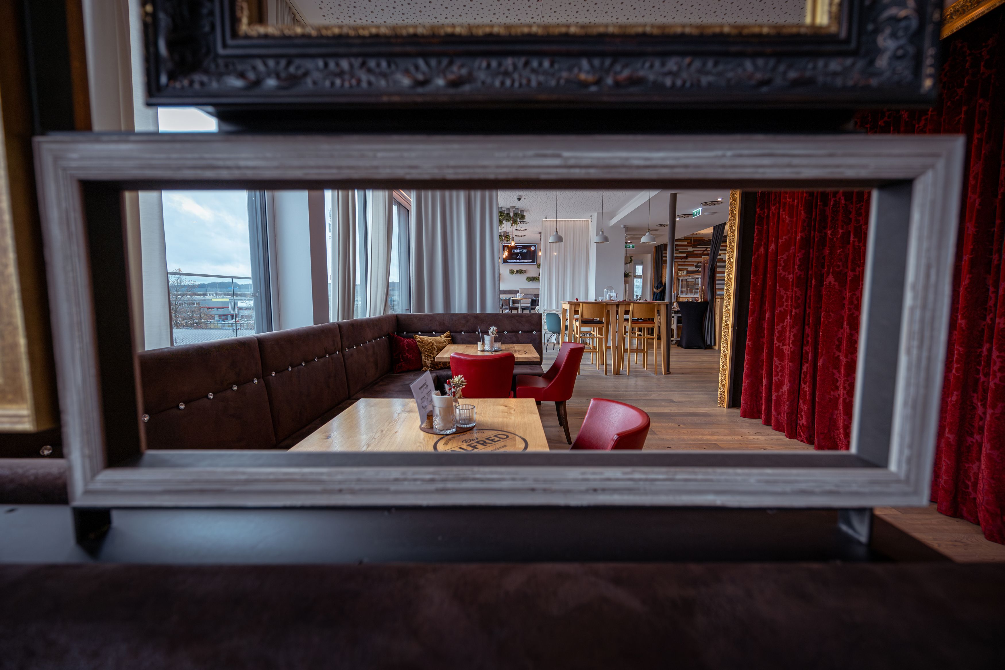 Interior view of a stylish café with red chairs and wooden tables, seen through a picture frame.