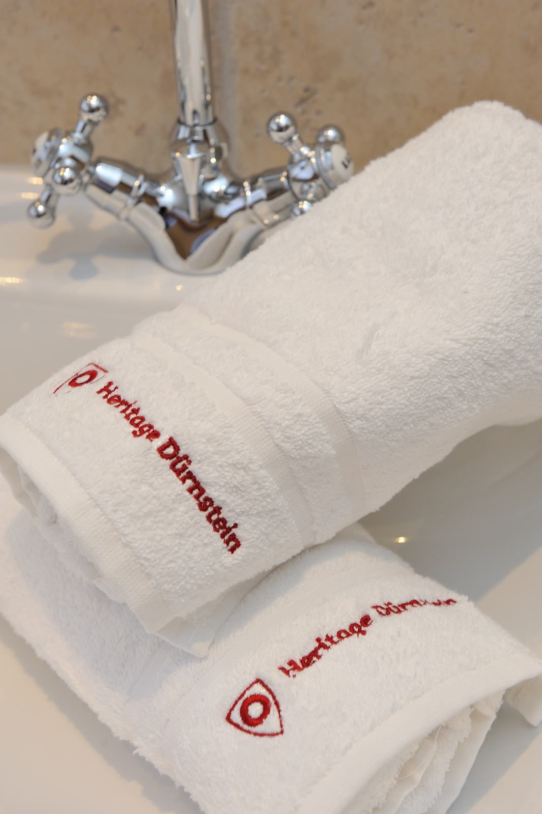 White towels with red lettering 'Heritage Dürnstein' on a washbasin with tap.