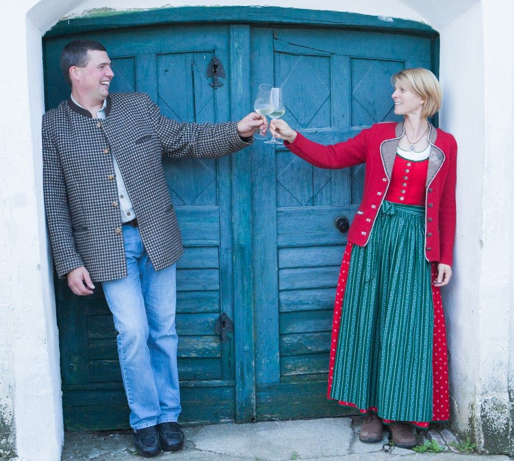 A man and a woman clink glasses of wine in front of a blue wooden door.
