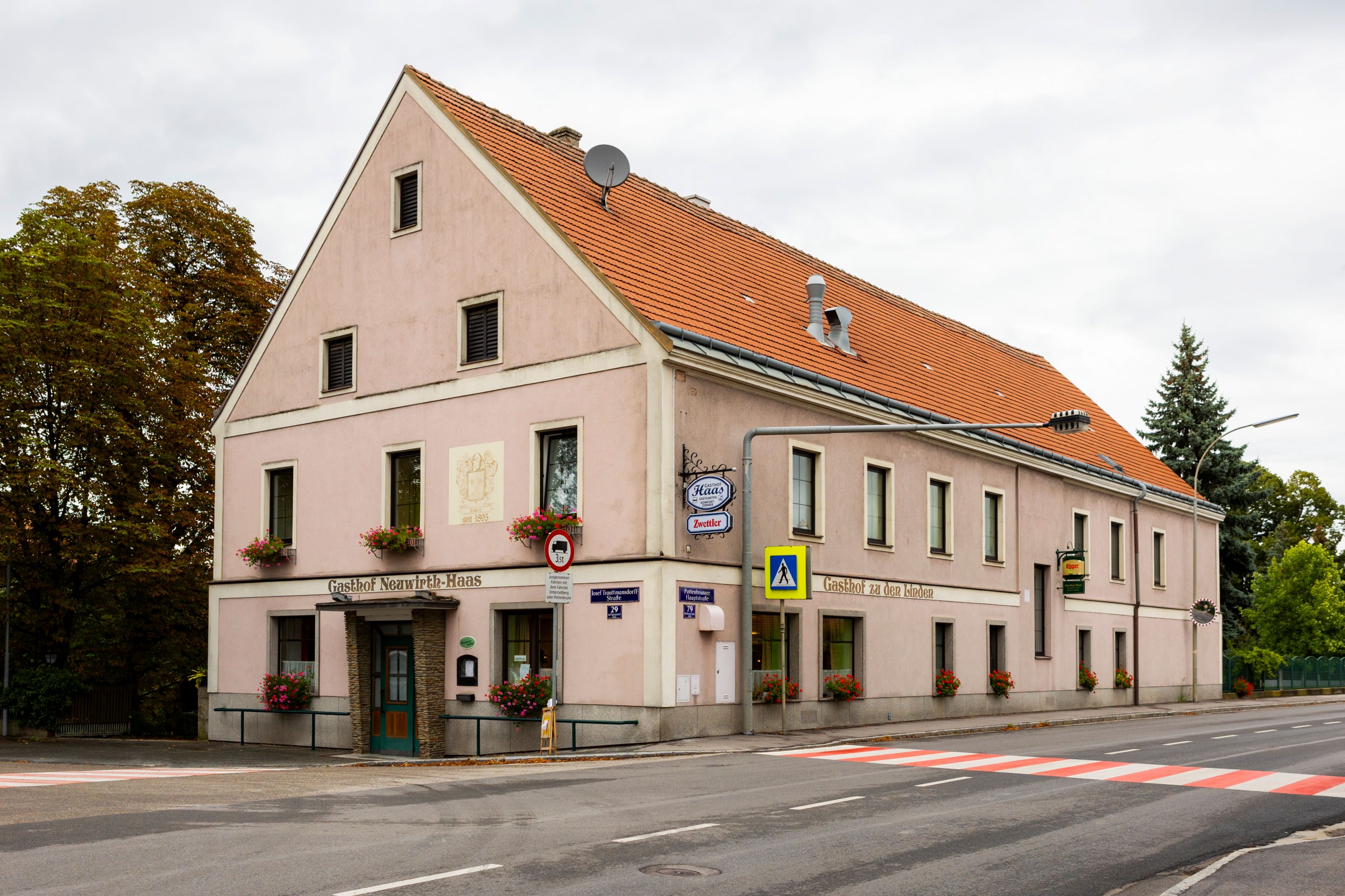 A traditional pub with a pink façade and red roof tiles on a street corner in Pottenbrunn.