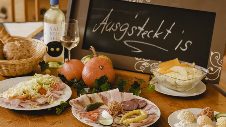 A laid table with cold plates, bread, wine and a sign saying 'Ausg'steckt is'.