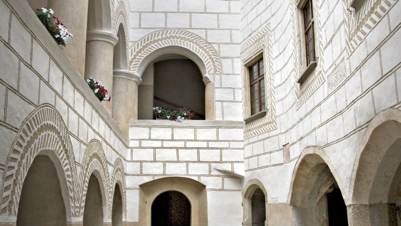 Historic arcaded courtyard with white walls and flowers in the window recesses.
