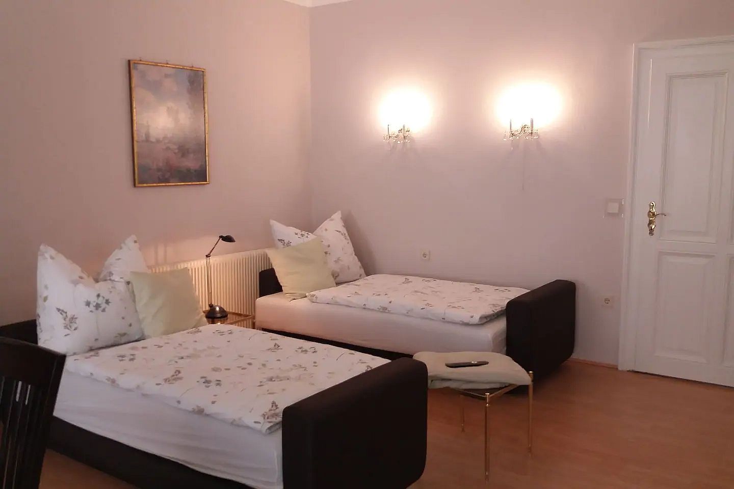 Two single beds in a bright room with wall lamps and a painting on the wall.