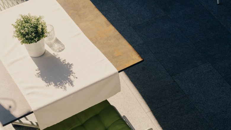 A table with a white tablecloth, potted plant and glass outside.