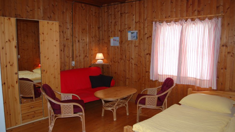 Interior view of a cozy room with wooden walls, red sofa, table, chairs and bed.
